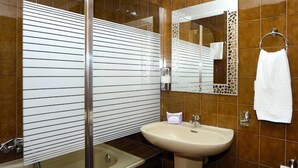 Un baño con cabina de ducha de vidrio, lavabo y espejo con marco decorativo.