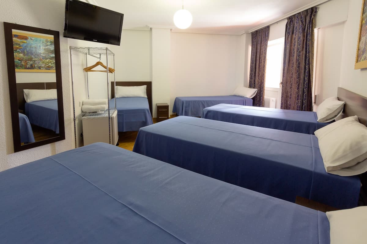 A hotel room with three single beds, a TV mounted on the wall, a mirror, and a hanging coat rack.