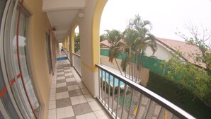 A corridor with a checkered floor, a balcony with a metal railing, and a view of a building with a tiled roof and palm trees. - Hotel Rio Balsas (Manzanillo)