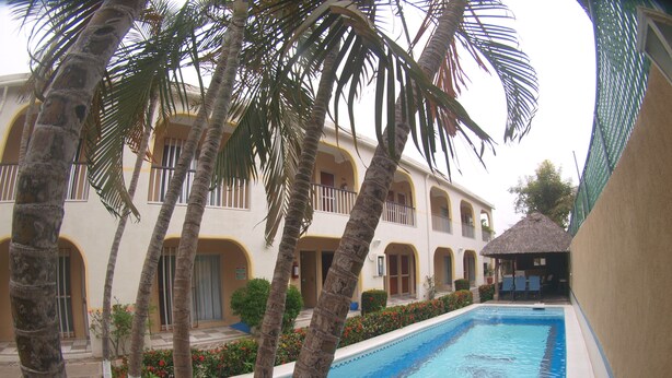 A pool area with palm trees, a building with balconies, and a thatched-roof structure. - Hotel Rio Balsas (Manzanillo)