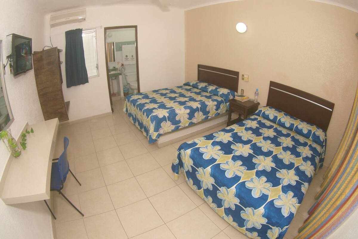A hotel room with two beds, a desk, a chair, and a ceiling fan.