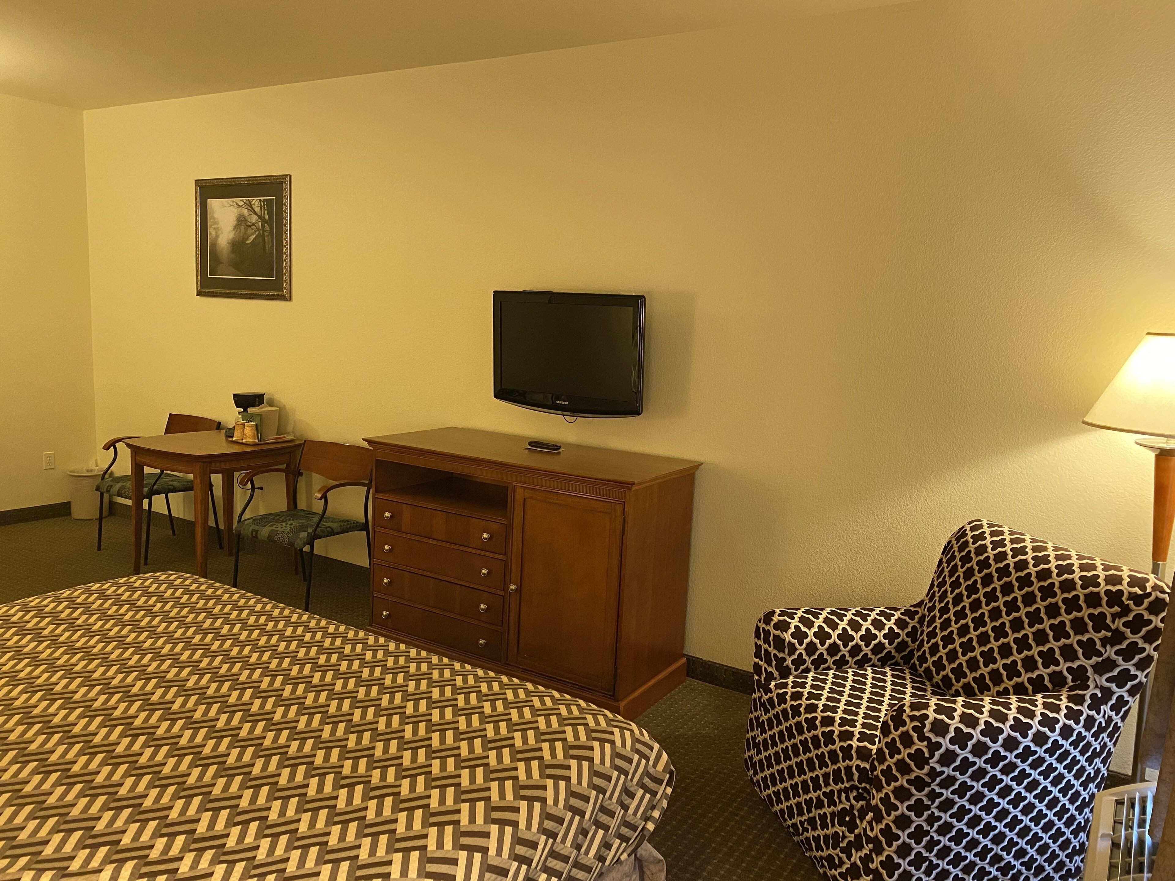 Ein Hotelzimmer mit einem Bett, einem Schreibtisch mit Stuhl, einem Fernseher und einem gemusterten Sessel.