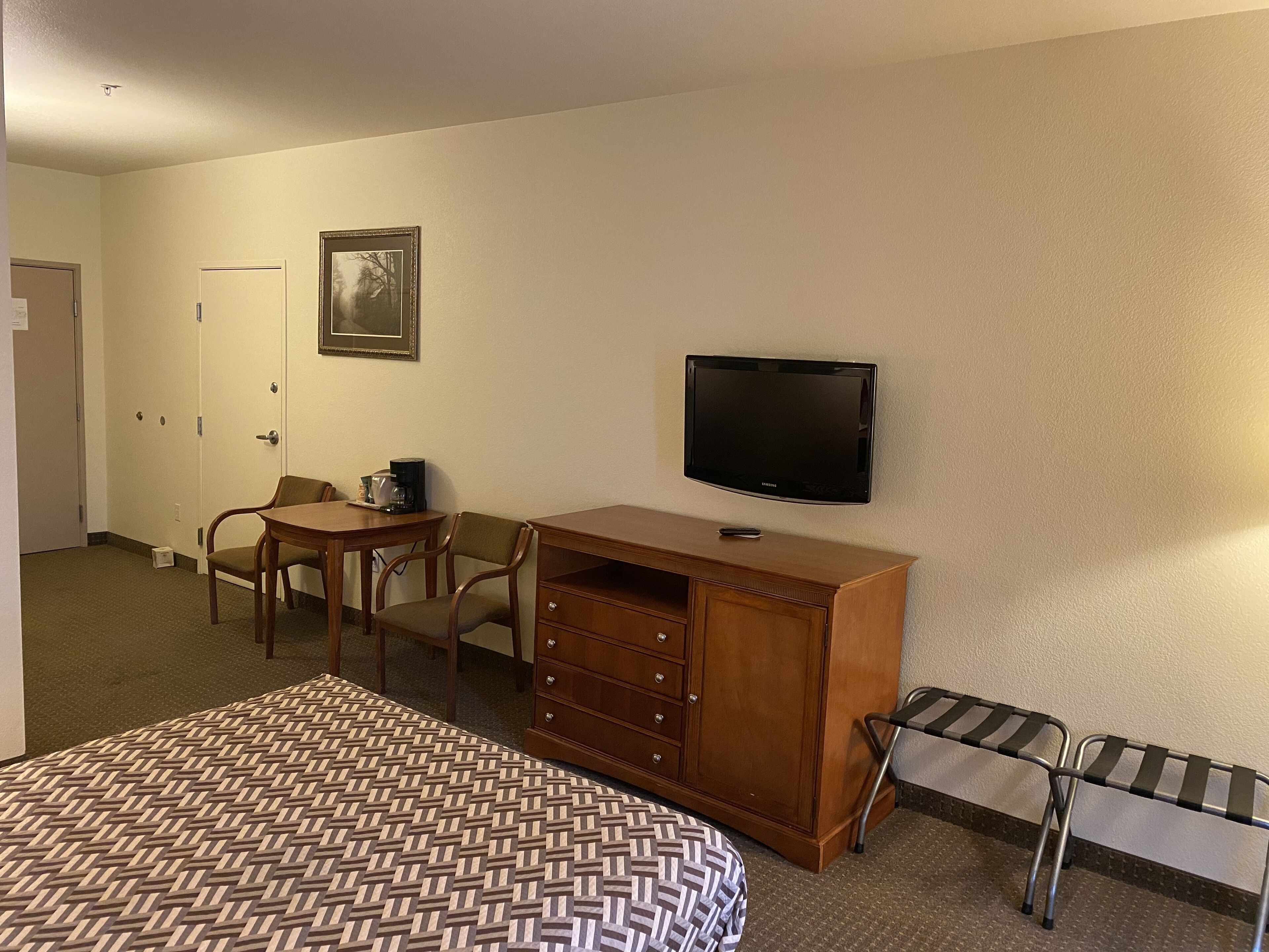 A hotel room with a bed, a desk with a chair, a television, and a small table with a coffee maker.