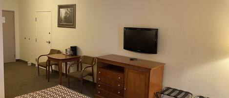 A hotel room with a bed, a desk with a chair, a television, and a small table with a coffee maker.