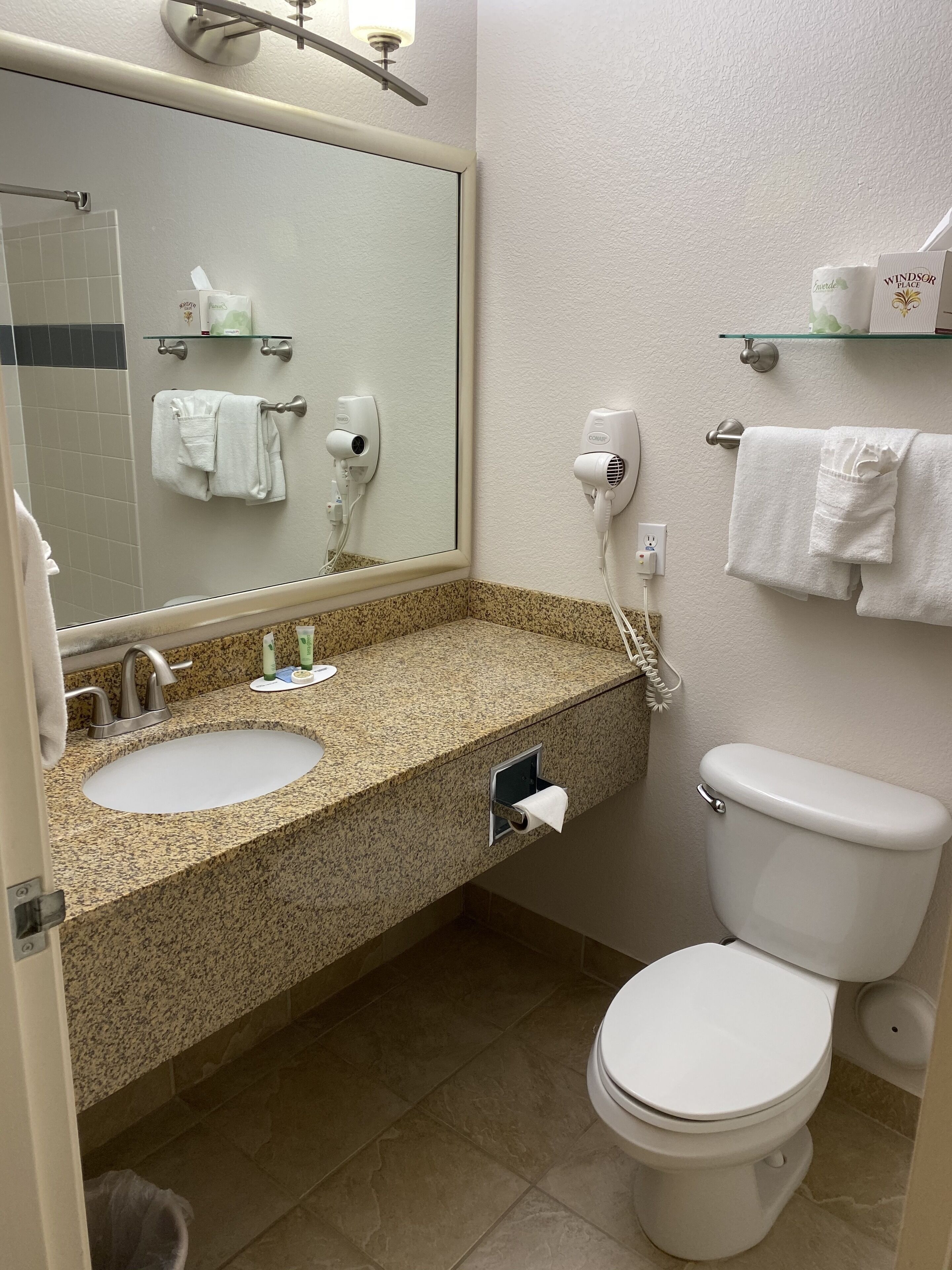 Un baño con dos lavamanos, un inodoro, un espejo y un perchero para toallas.