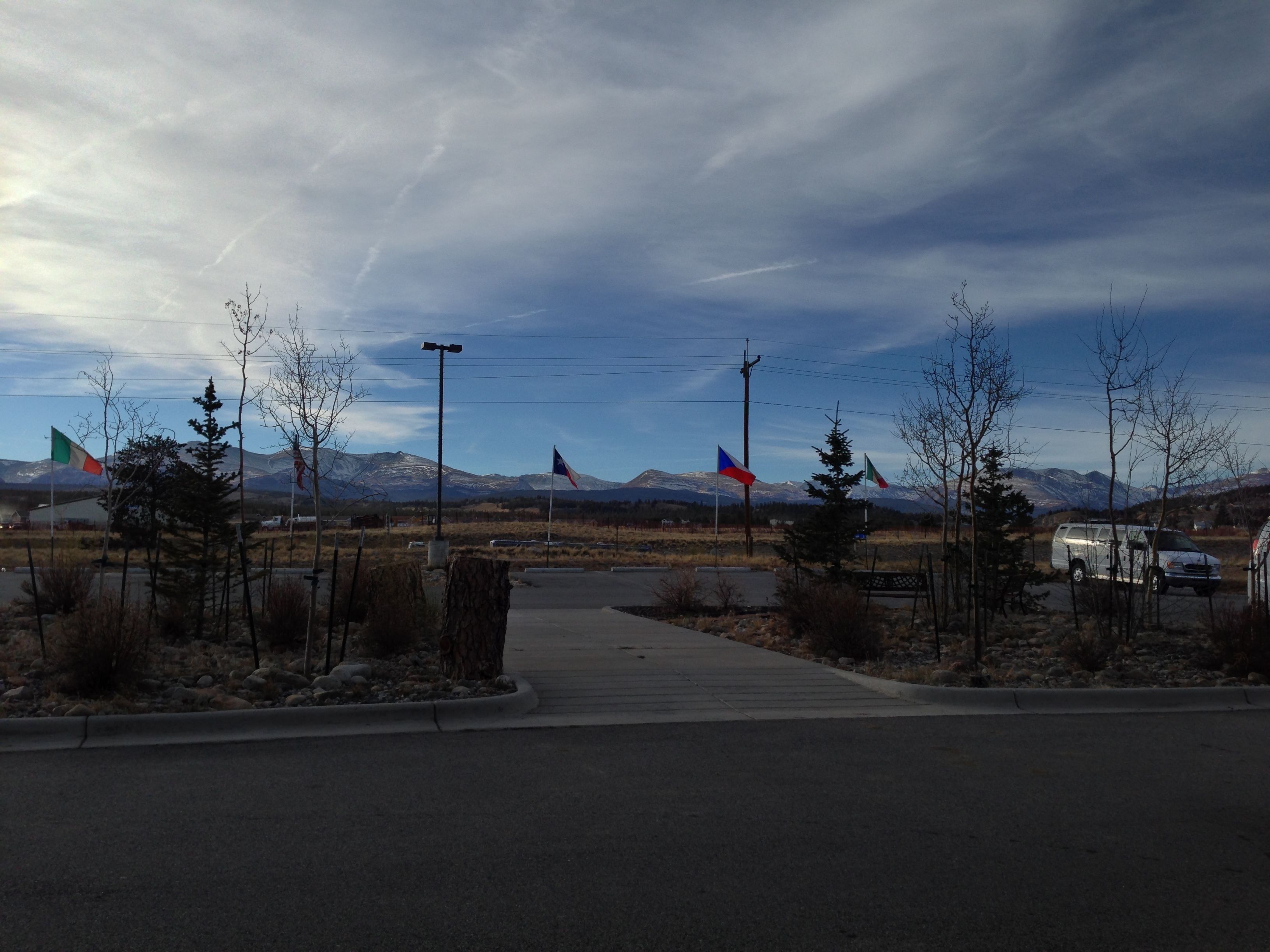 A parking area with multiple flags, a paved walkway, and a mountainous backdrop.