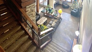 A spacious living area with a wooden staircase, a fireplace, and a large window with multiple panes.