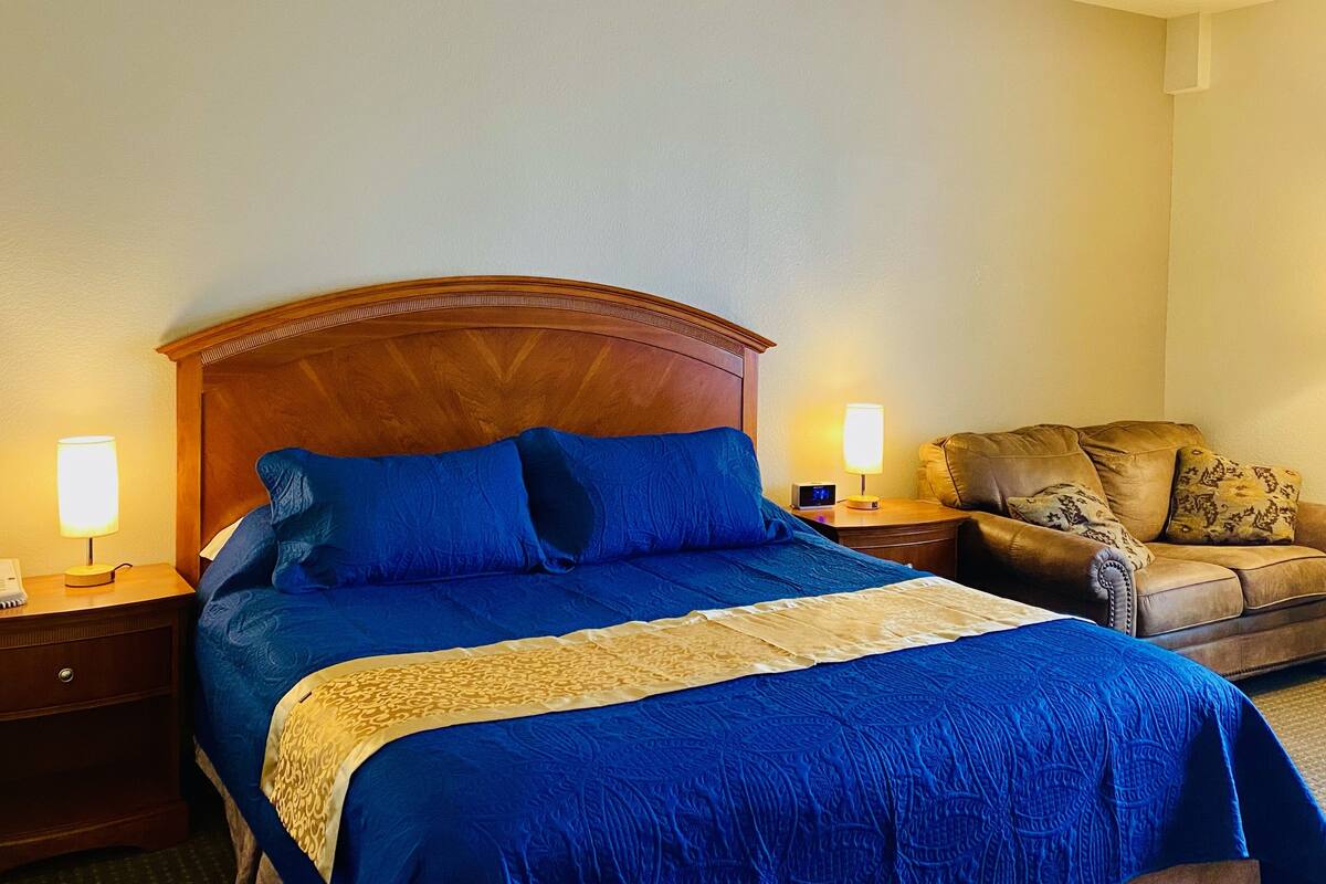 A hotel room with a large bed, two bedside lamps, a leather armchair, and a small table with a lamp.