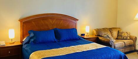 A hotel room with a large bed, two bedside lamps, a leather armchair, and a small table with a lamp.