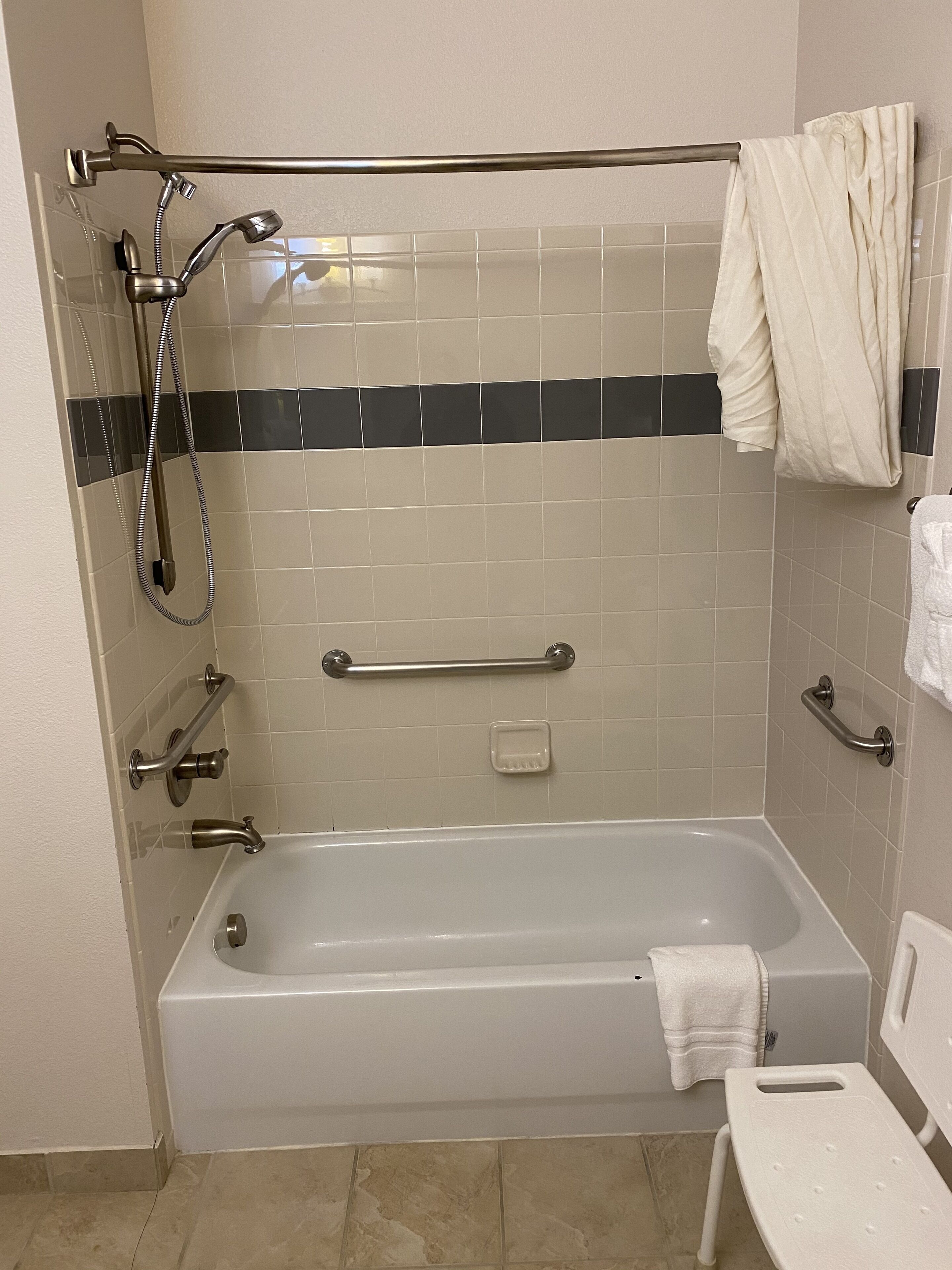 A standard bathroom with a bathtub, a shower, grab bars, and a towel rack.
