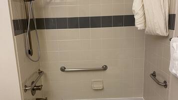 A standard bathroom with a bathtub, a shower, grab bars, and a towel rack.