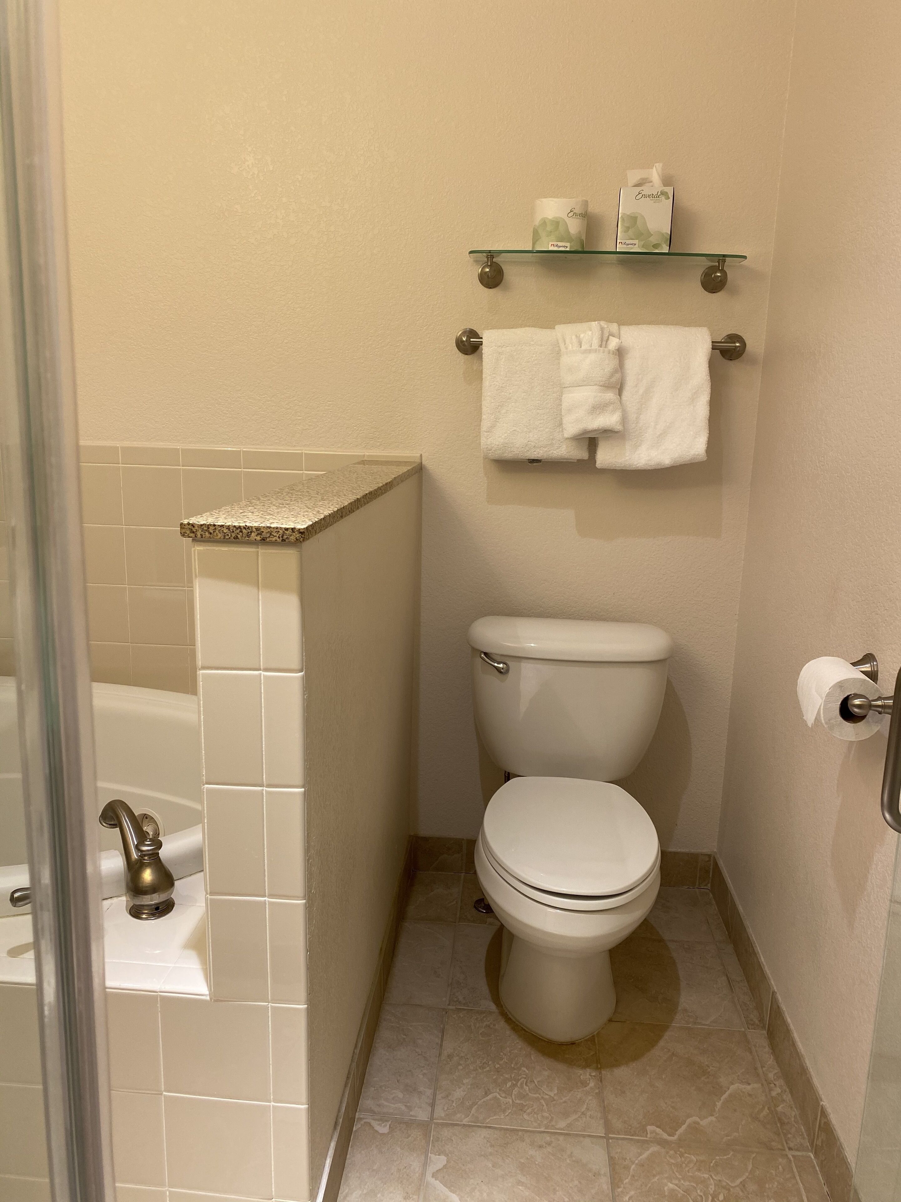 Un baño con inodoro, un estante de vidrio con artículos de aseo y zona de ducha.