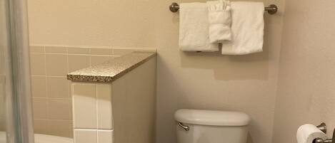 Un baño con inodoro, un estante de vidrio con artículos de aseo y zona de ducha.