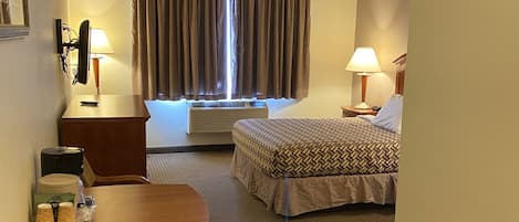Habitación de hotel con cama, escritorio con silla, mesa, lámpara y ventana con cortinas.