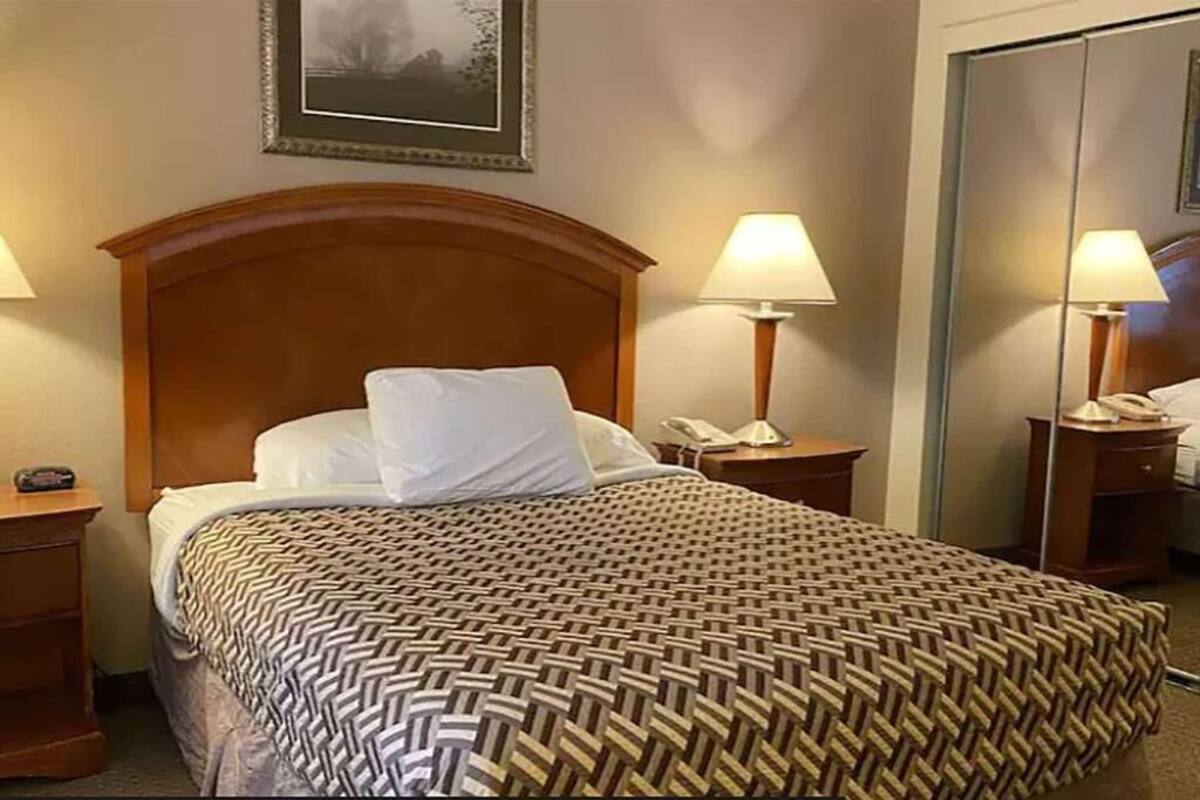 A hotel room with a wooden headboard, two bedside lamps, a telephone, a mirror, and a patterned bedspread.