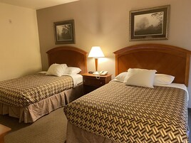 A hotel room with two beds, each with a wooden headboard, a nightstand with a lamp, and framed pictures on the wall.