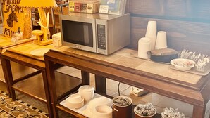 A table with a microwave, paper plates, cups, and a lamp.