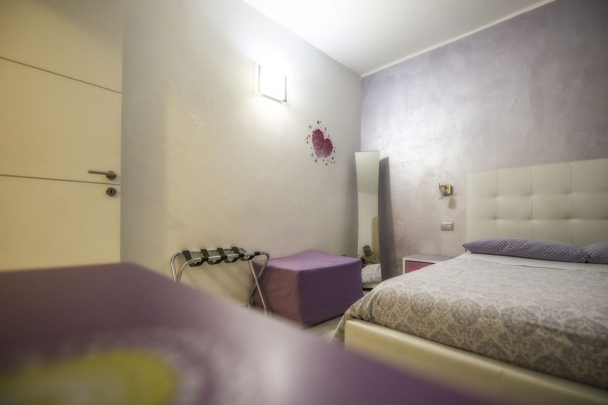 A bedroom with a bed, a nightstand, a mirror, and a door.