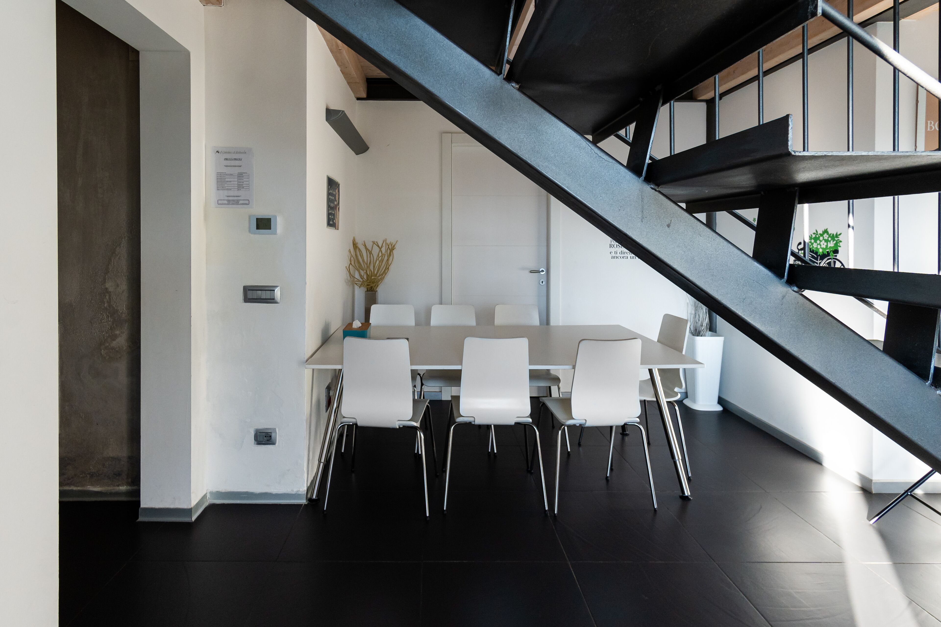 Un comedor moderno con una mesa larga y sillas blancas, una escalera y una puerta con un letrero.