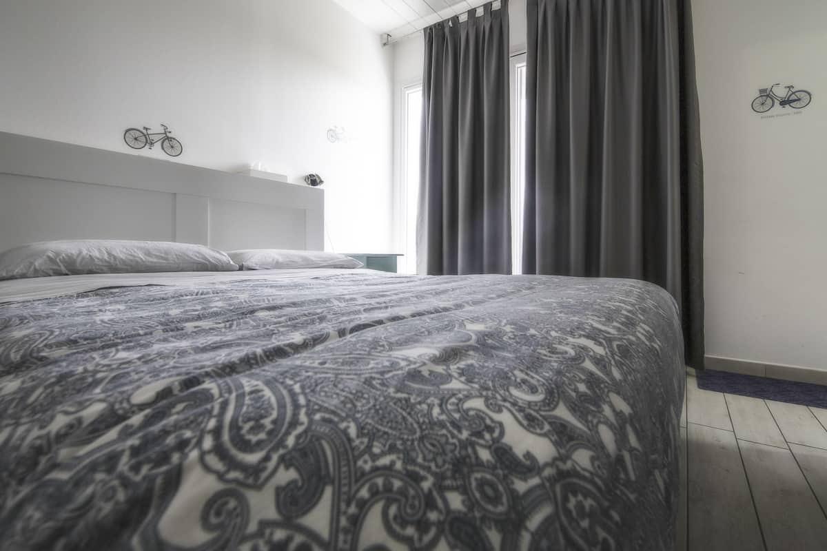 A modern hotel room with a large bed, a headboard, a window with curtains, and wall decorations including a bicycle.
