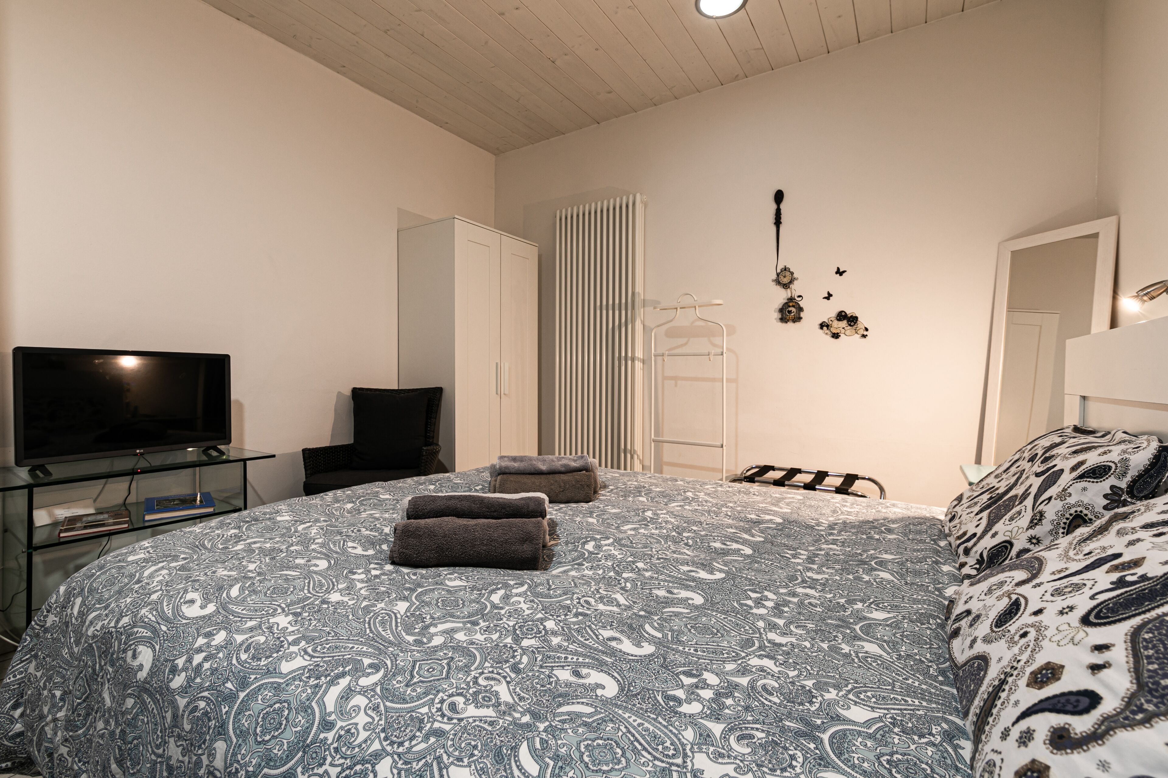 Een slaapkamer met een groot bed, een televisie op een glazen plank, een kledingkast en een radiator.