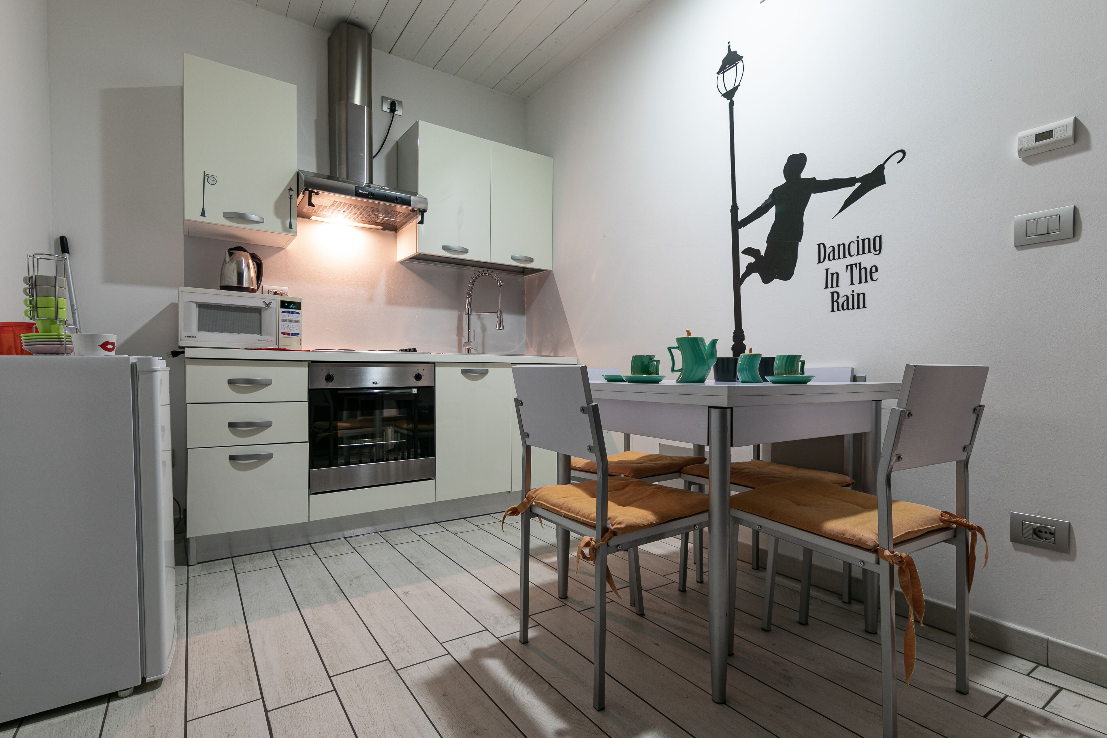 A modern kitchen with white cabinets, a microwave, and a stove. There is a dining table with chairs and a wall decal of a dancing figure.