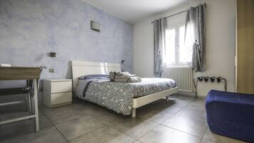 A bedroom with a bed, a desk, a chair, a radiator, and a window with curtains.
