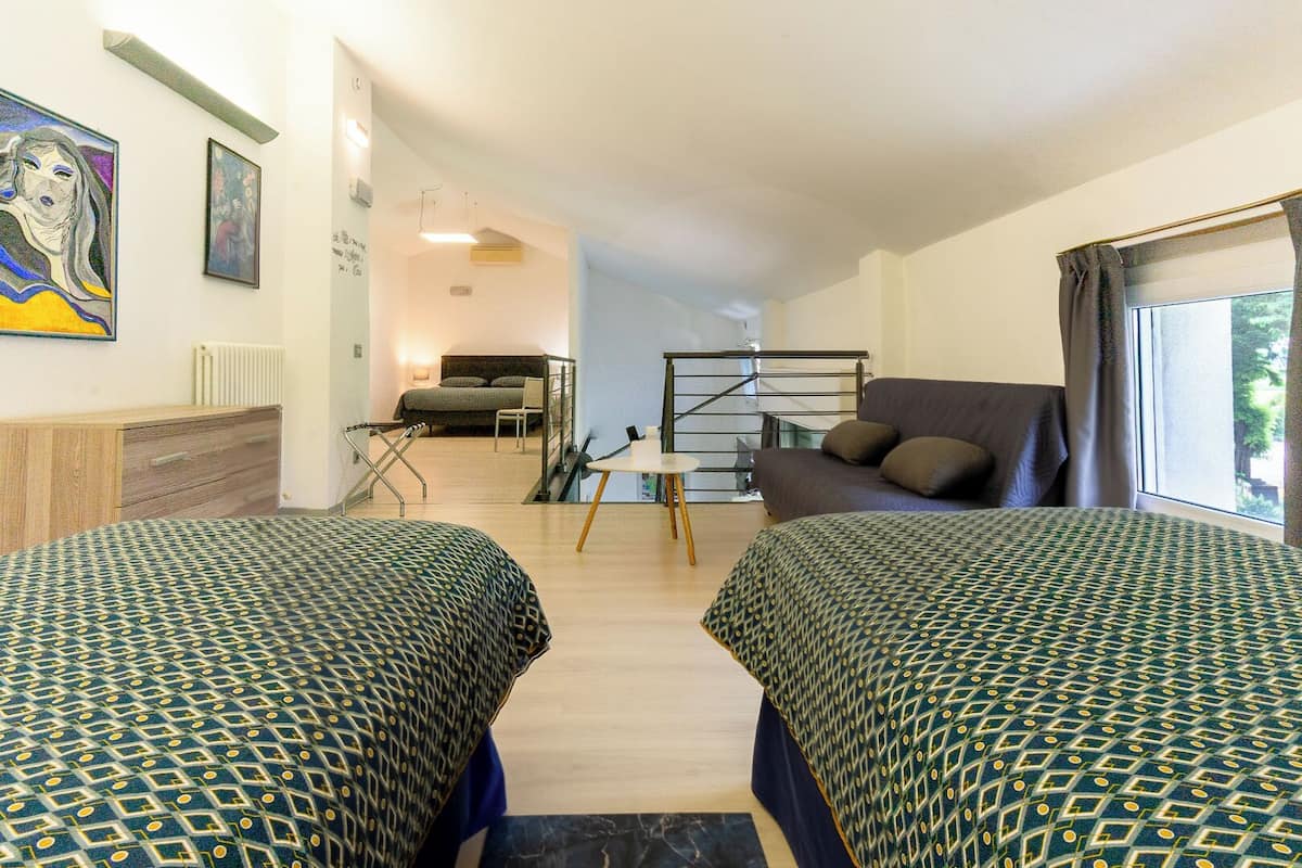 A room with two beds, a sofa, a desk, and a staircase.