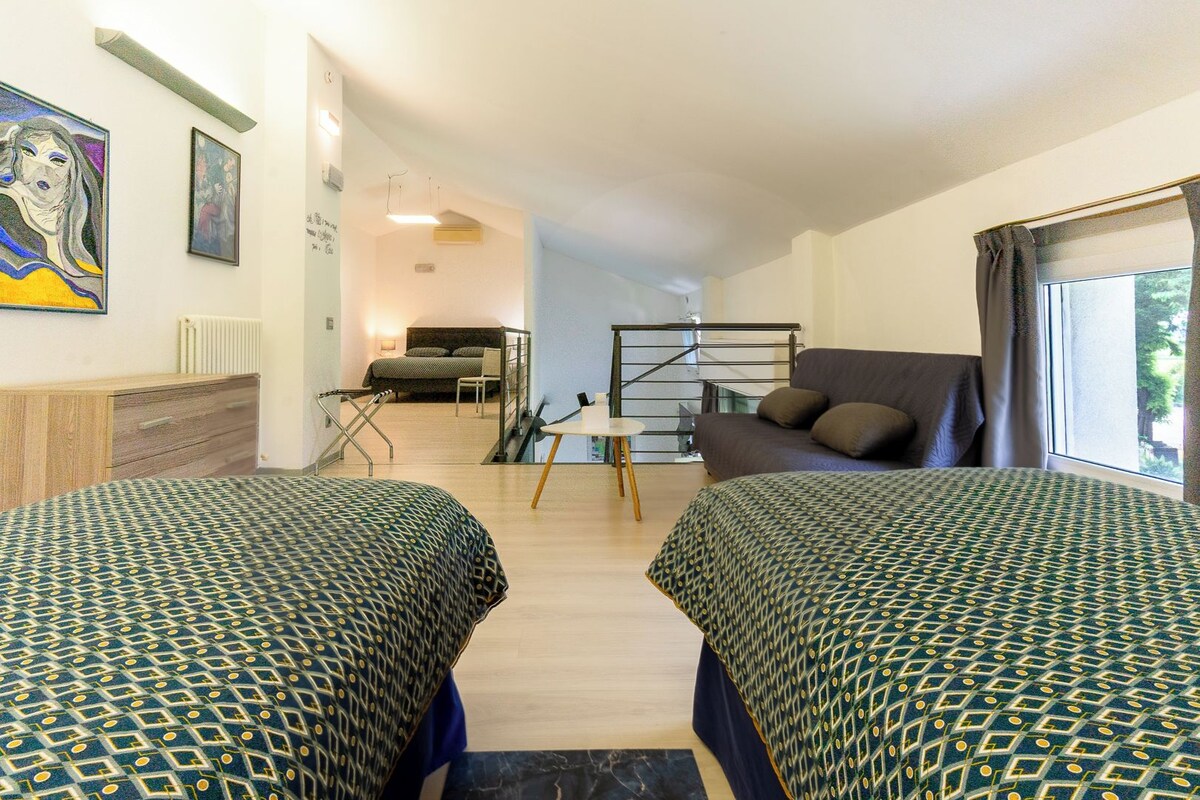 Quarto com duas camas, um sofá, uma escrivaninha e uma escada.