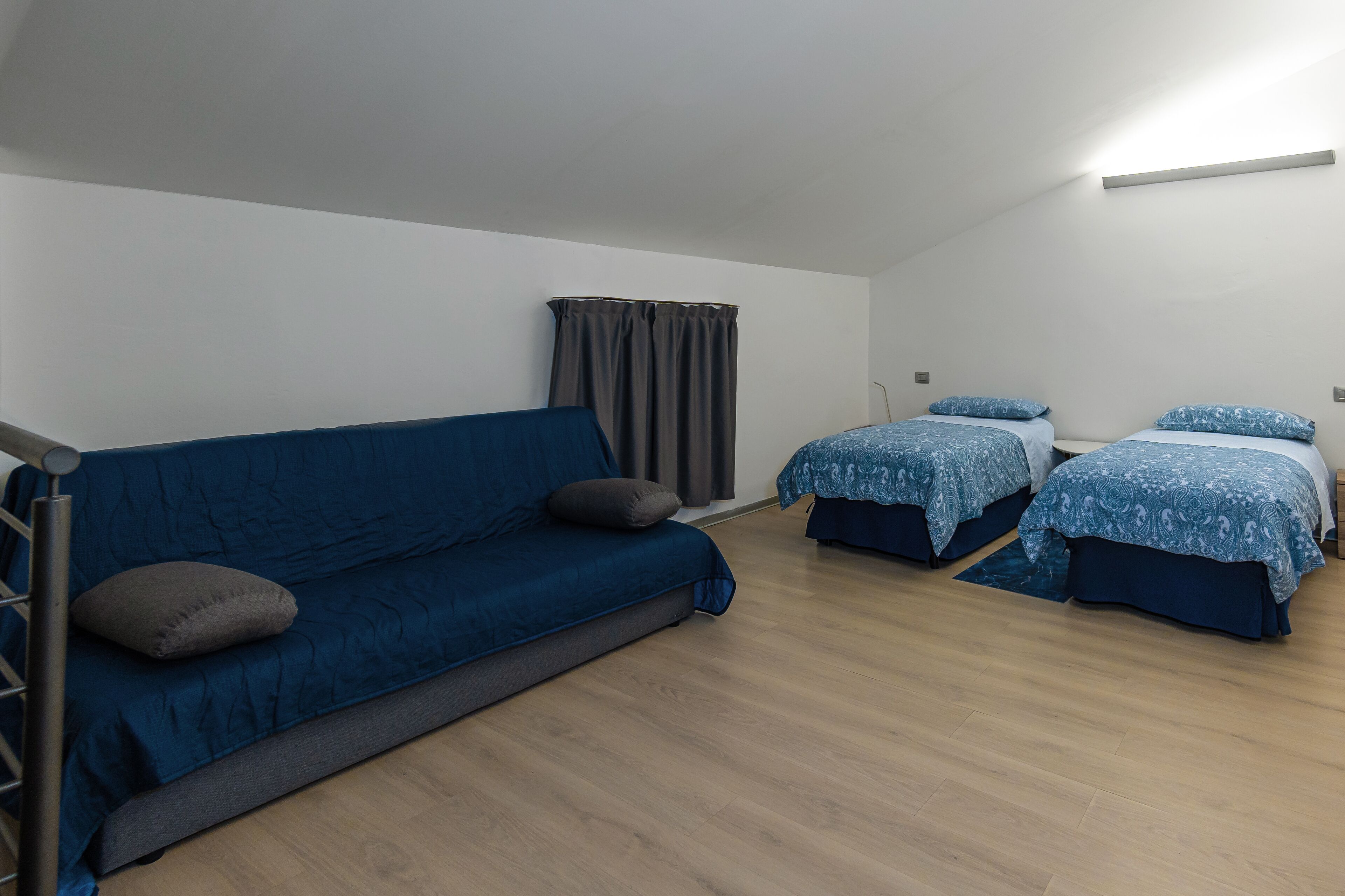 Una stanza con un divano blu, due letti con copriletto decorato, una tenda e un lampadario.