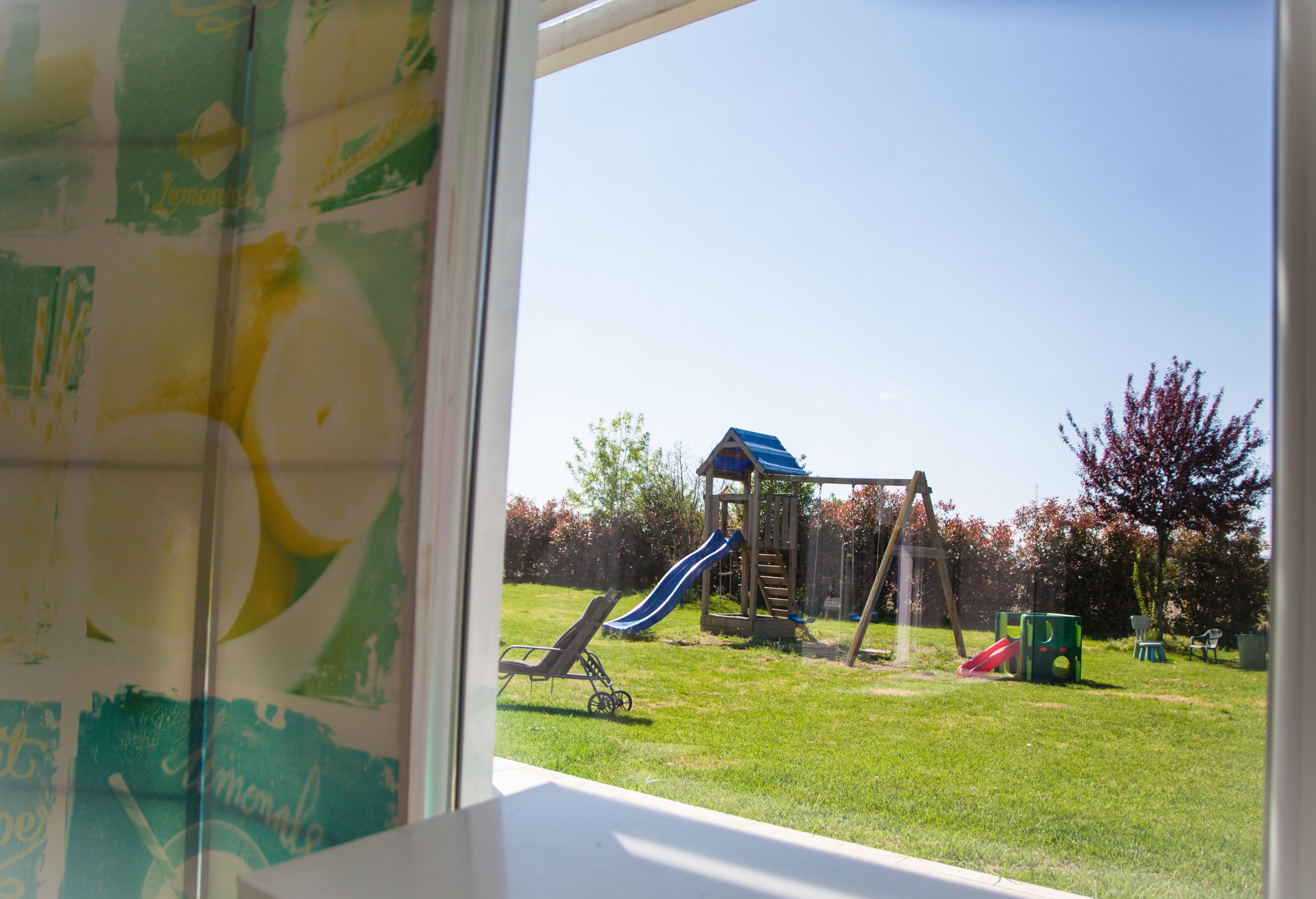 A view of a playground with a slide and swings through a window.