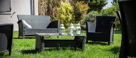 An outdoor seating area with wicker furniture and a table, surrounded by greenery.