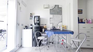 A compact kitchen with a coffee machine, a sink, and a small dining area with a table and chairs.