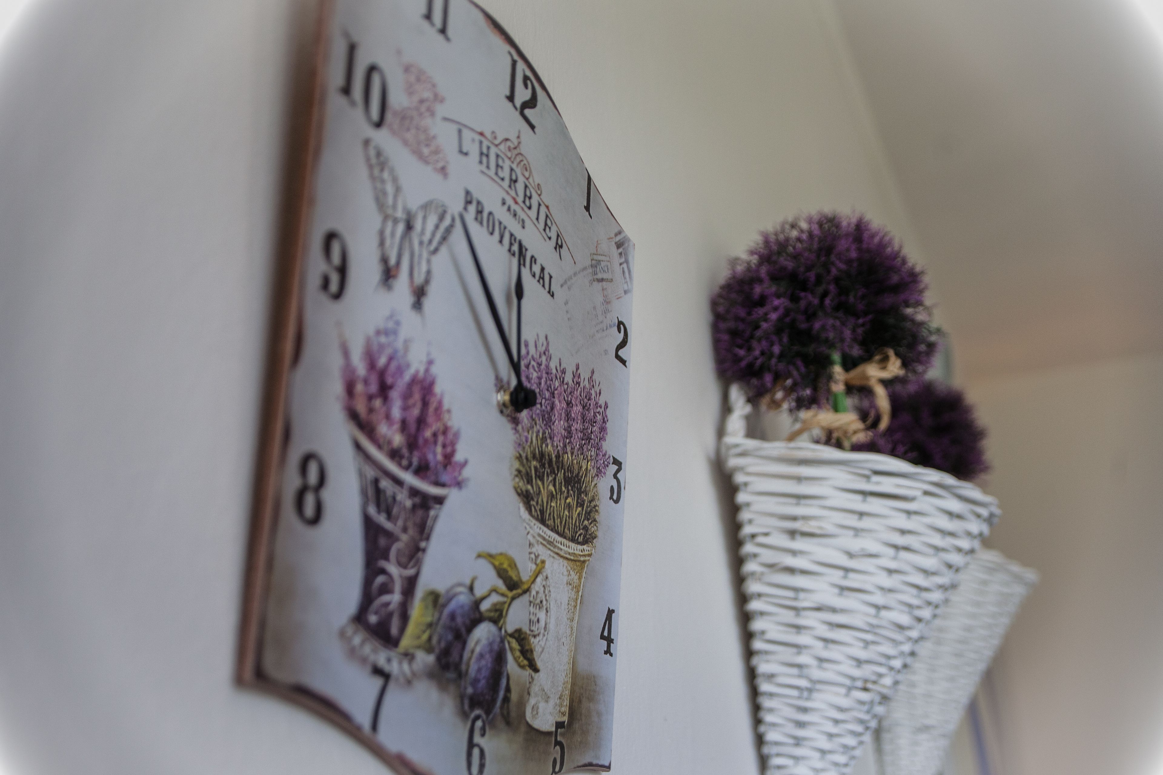 A wall clock with floral designs and a wicker basket with purple flowers.
