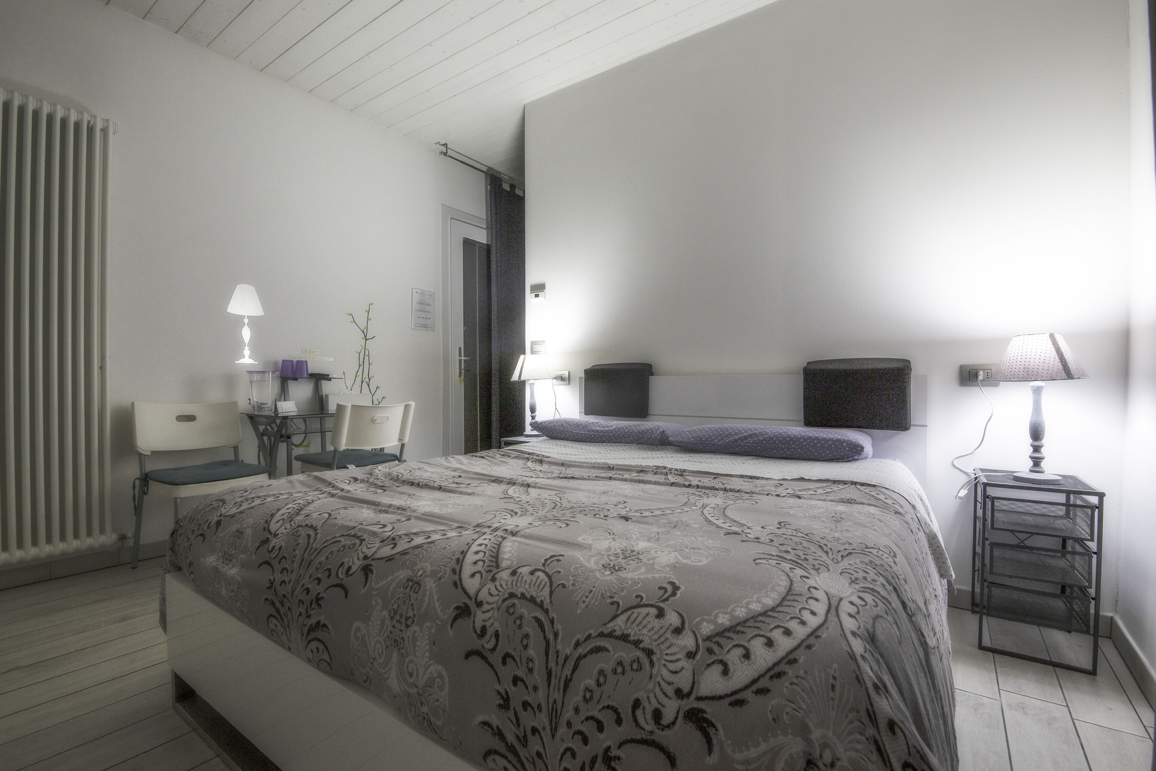 A bedroom with a large bed, a desk with a chair, a lamp, and a radiator.
