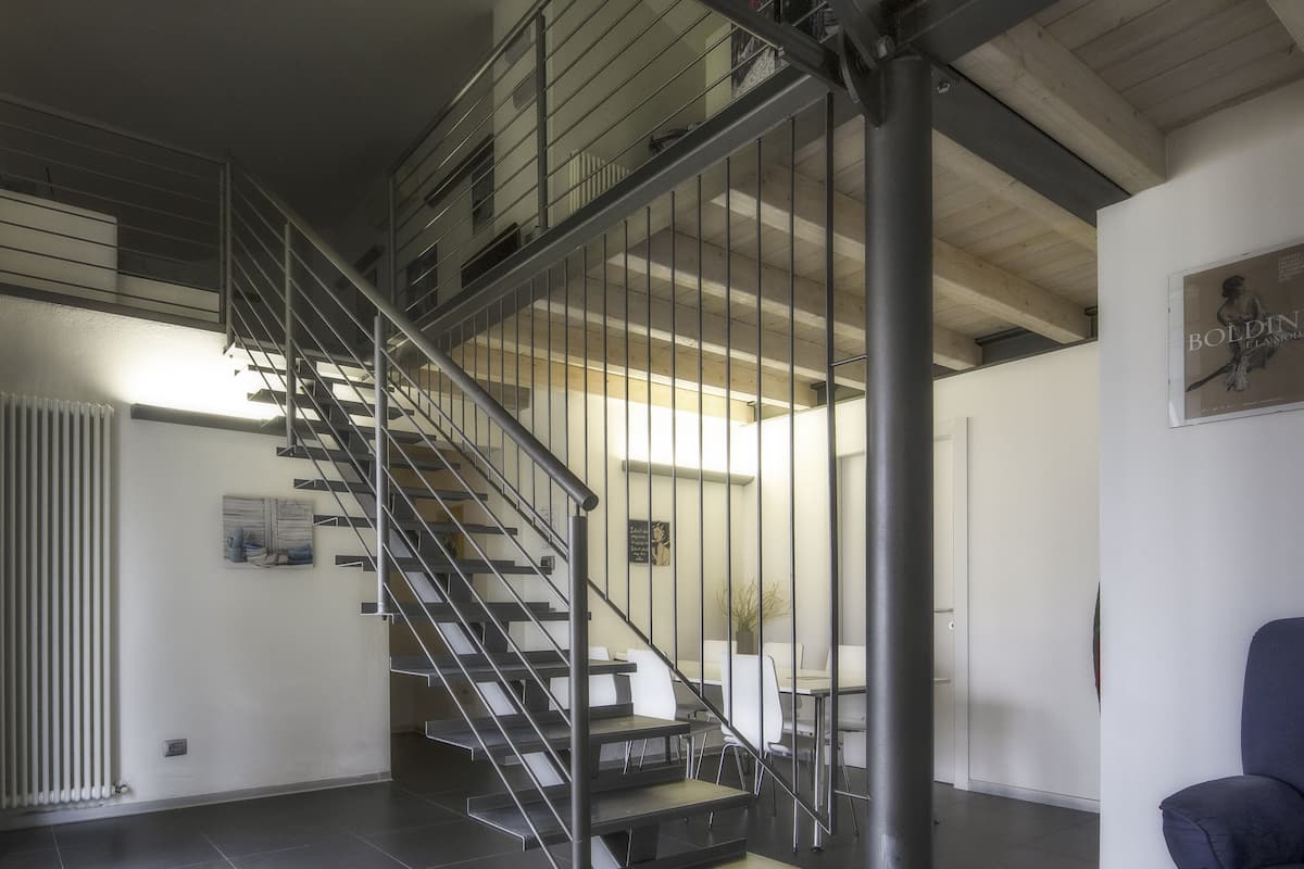 A modern interior with a staircase leading to an upper level, a dining area with white furniture, and a poster on the wall.