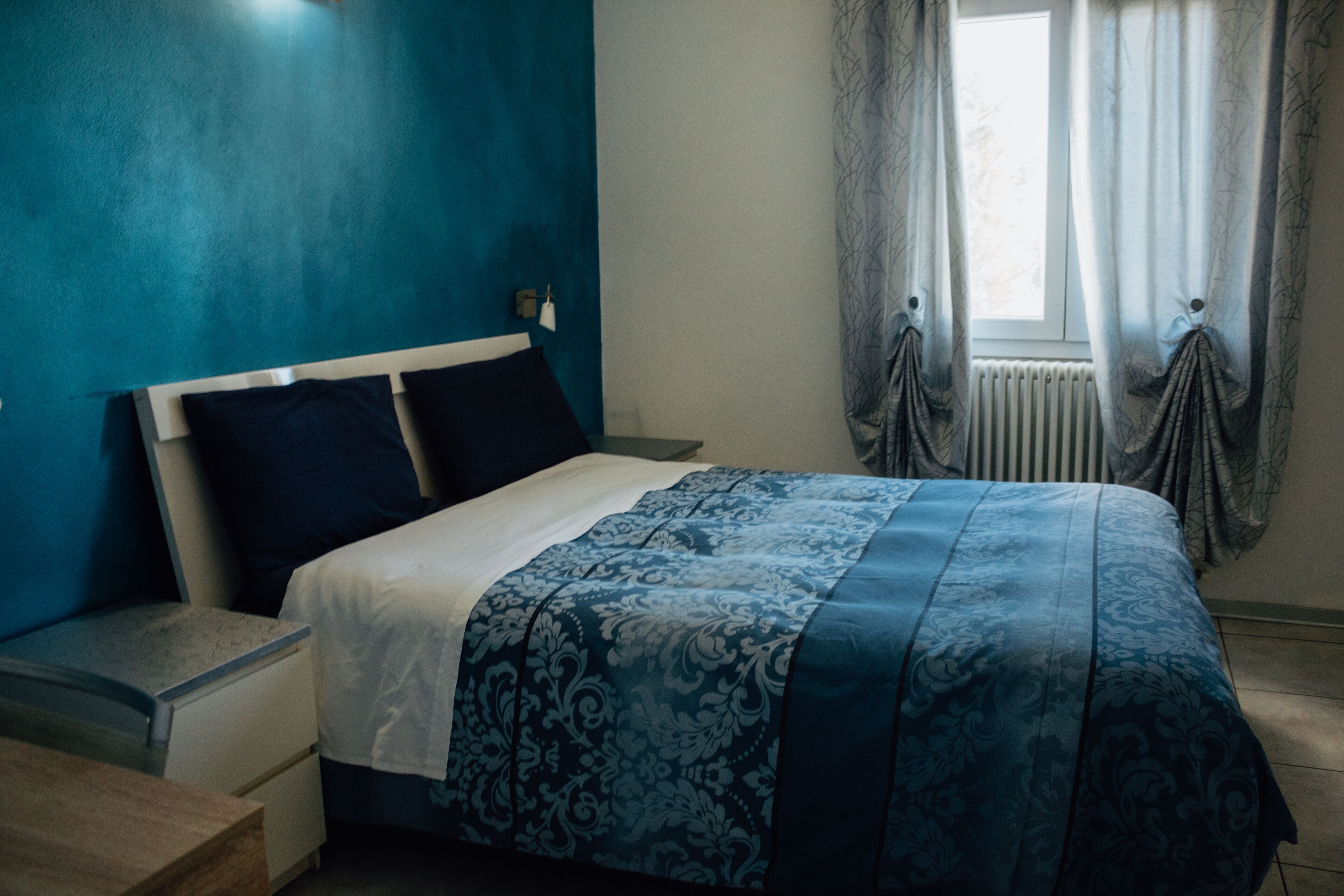 A bedroom with a bed, nightstand, and a window with curtains.