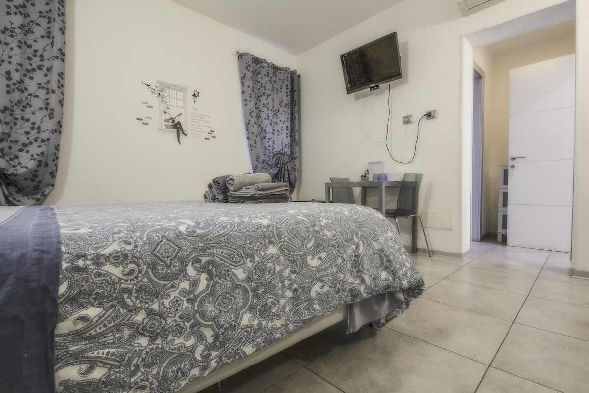 A bedroom with a bed, a desk, a chair, a TV, and a door.