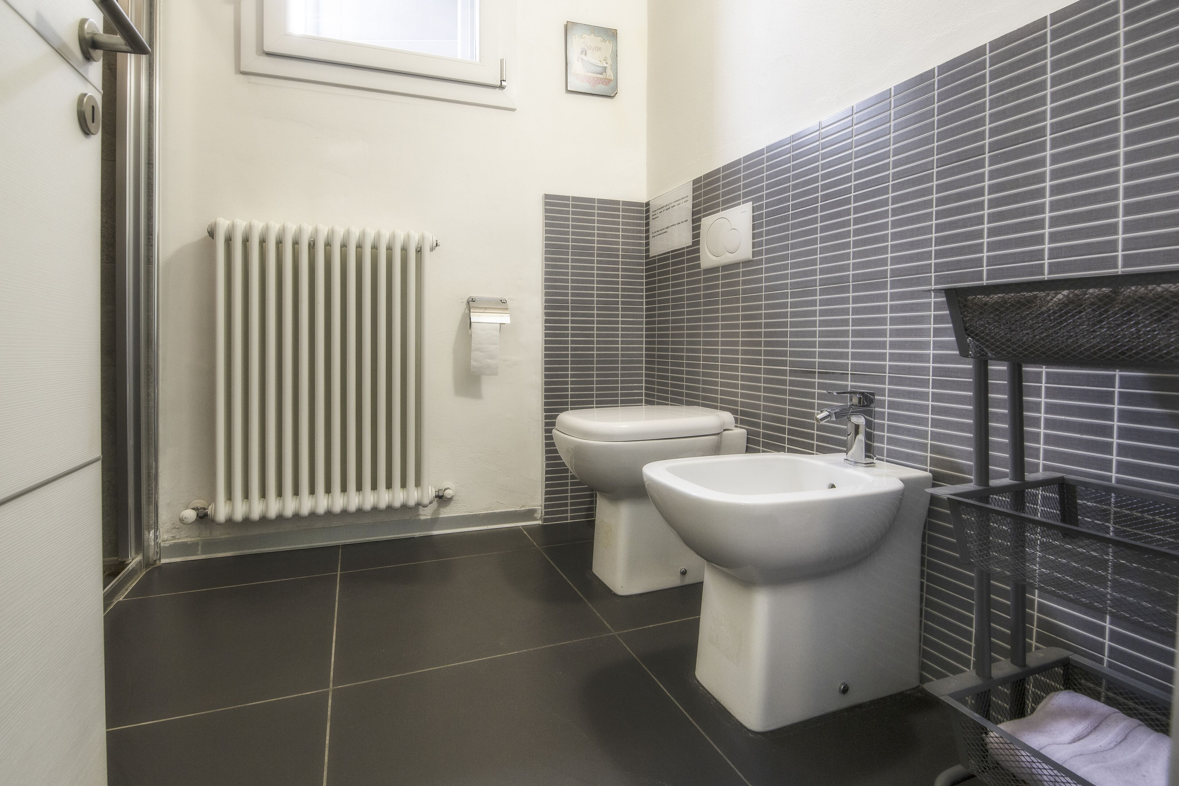 Un baño moderno con dos inodoros, un lavabo, un radiador y una zona de ducha.