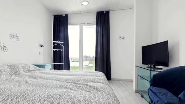 A modern hotel room with a large bed, a TV, and a view of a swimming pool.