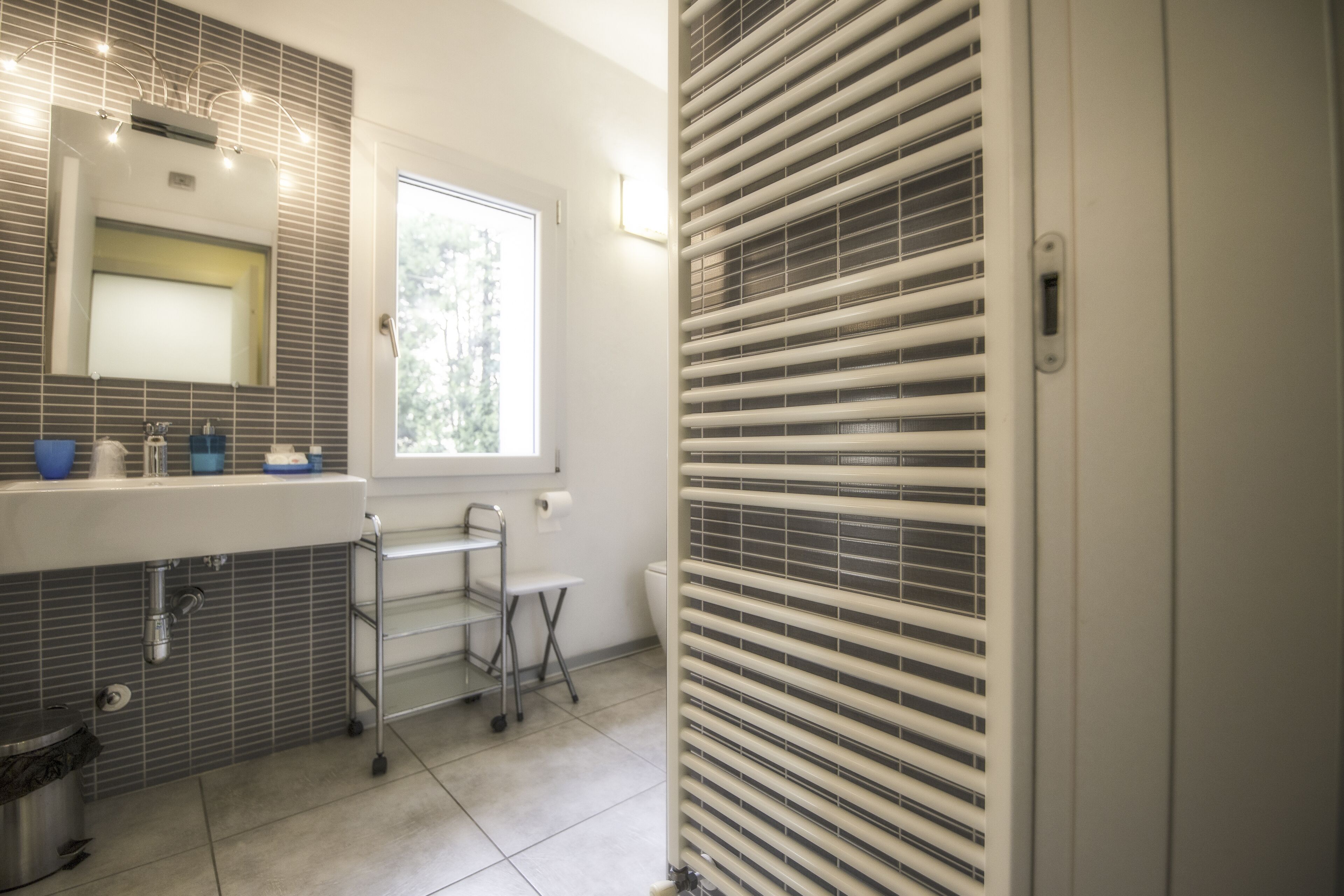 A modern bathroom with a large mirror, a sink with a chrome faucet, a window, and a toilet.