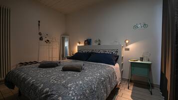 Une chambre à coucher avec une couvre-lit à motifs, une table de chevet avec une lampe et une illustration de vélo accrochée au mur.