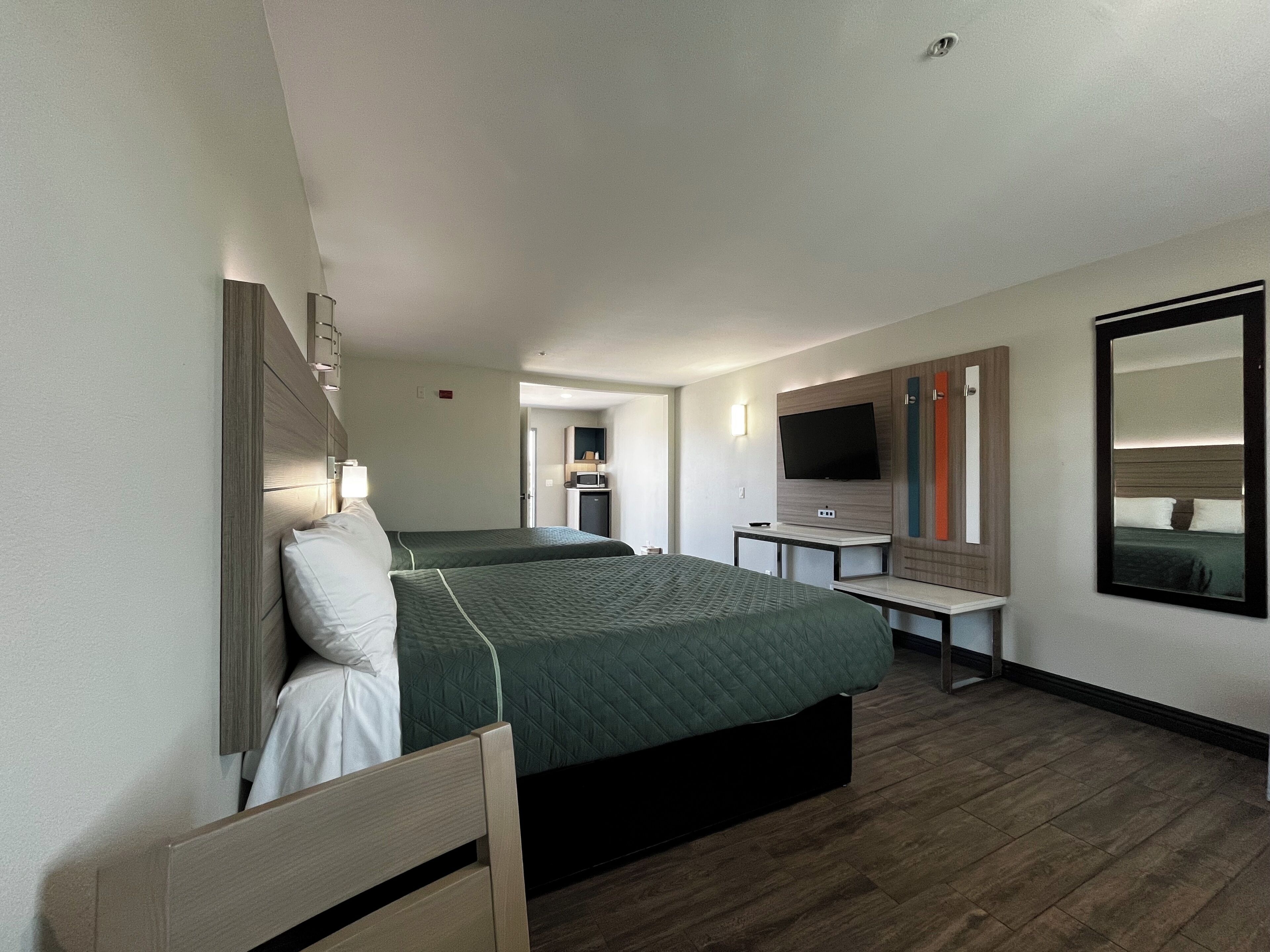 Ein Hotelzimmer mit zwei Betten, einem Schreibtisch, einem Fernseher und einem Spiegel.