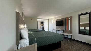 Ein Hotelzimmer mit zwei Betten, einem Schreibtisch, einem Fernseher und einem Spiegel.
