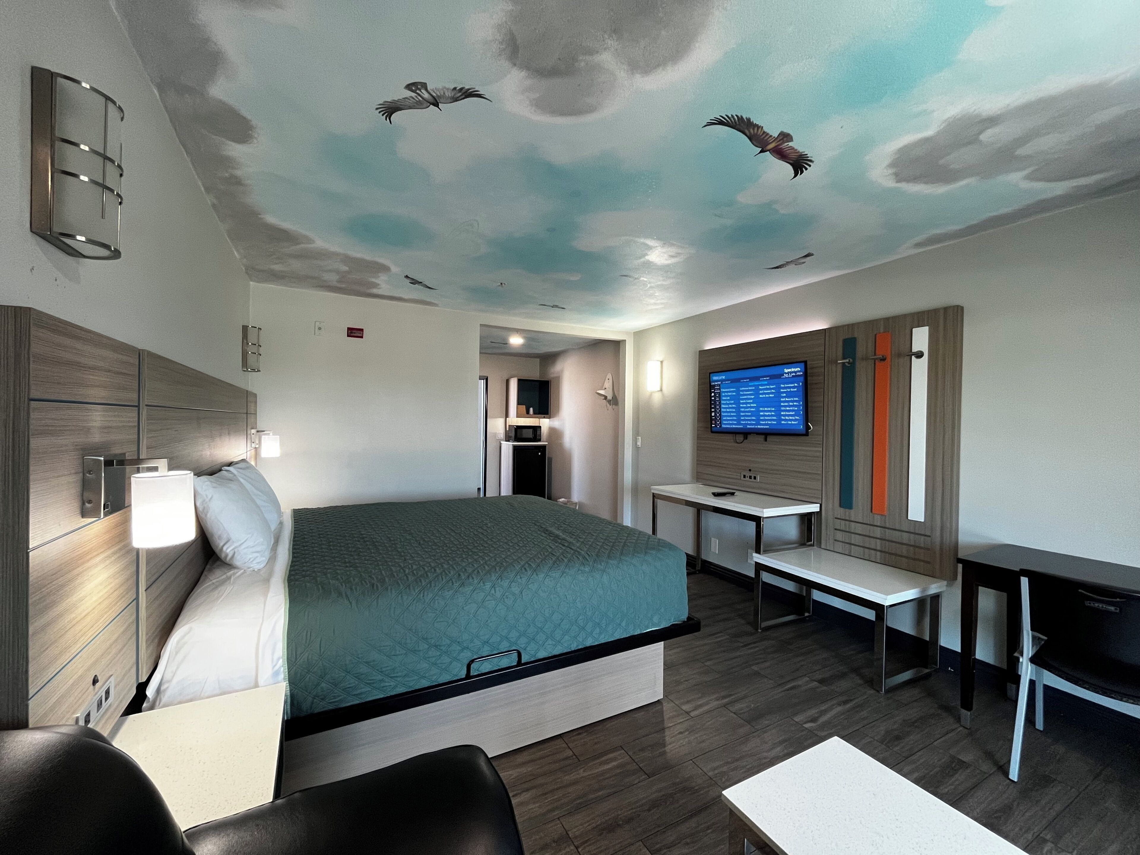 Habitación de hotel con cama, escritorio, televisor y un mural en el techo.
