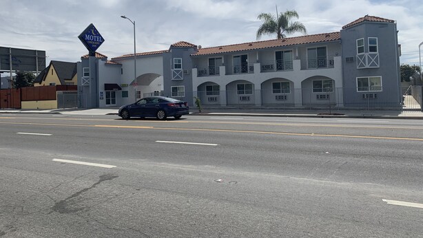 Un motel con un edificio de dos pisos, un automóvil estacionado al frente y un cielo despejado.