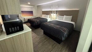 Habitación de hotel con dos camas, un escritorio, un microondas y una ventana con persianas.
