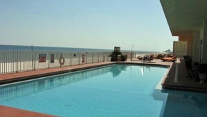Una piscina con vistas al océano, una valla blanca y sillas de descanso.