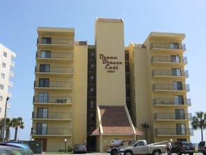 A multi-story hotel named Ocean Breeze East with a prominent vertical sign, balconies on each floor, and a parking area in front. - Tern Key Realty & Rentals (Pensacola)