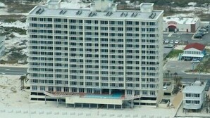 Un hotel grande con varios pisos, piscina y una playa al frente.